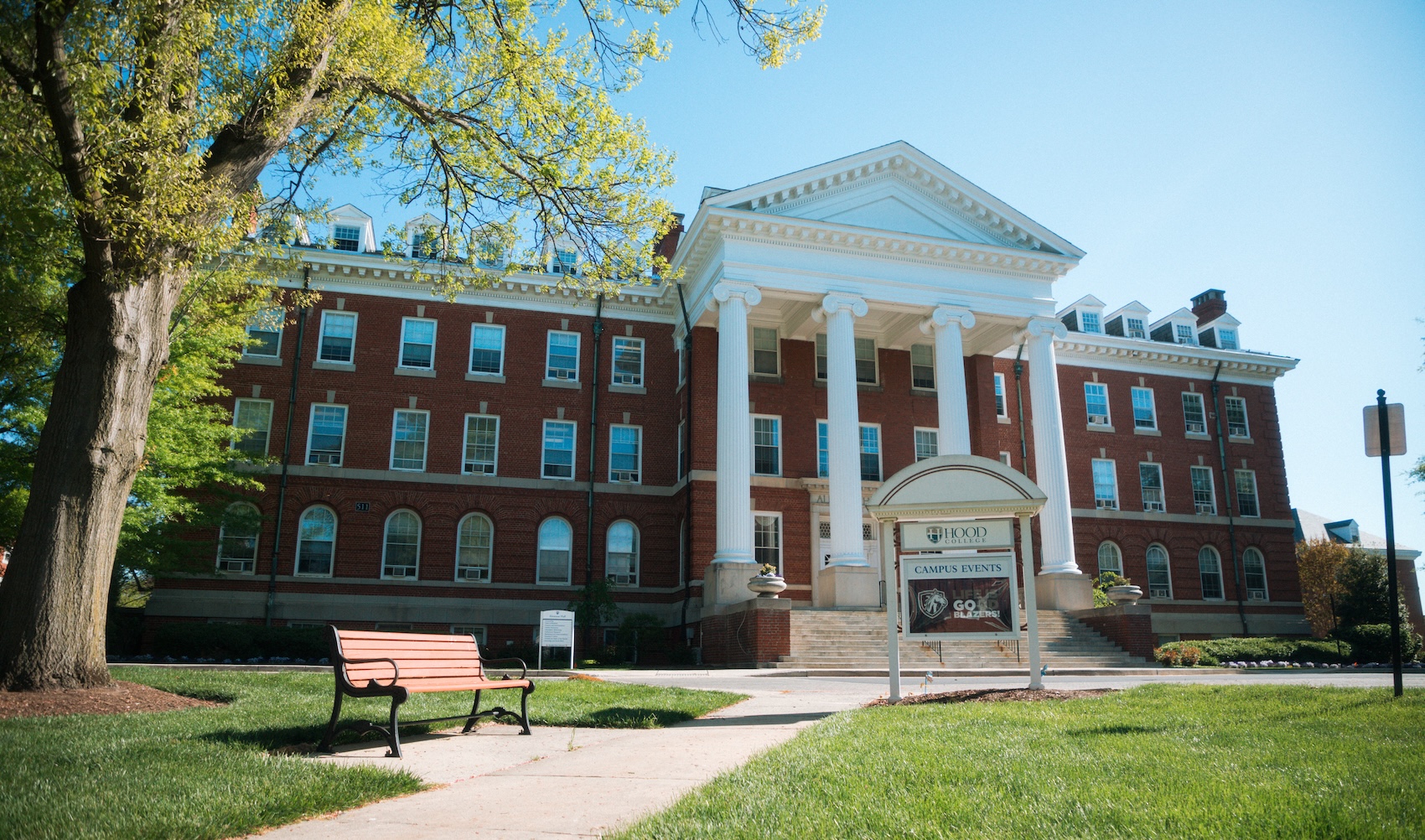 A photo of Alumnae Hall during a sunny day, with a sign that reads "Go Blazers!" in front. 