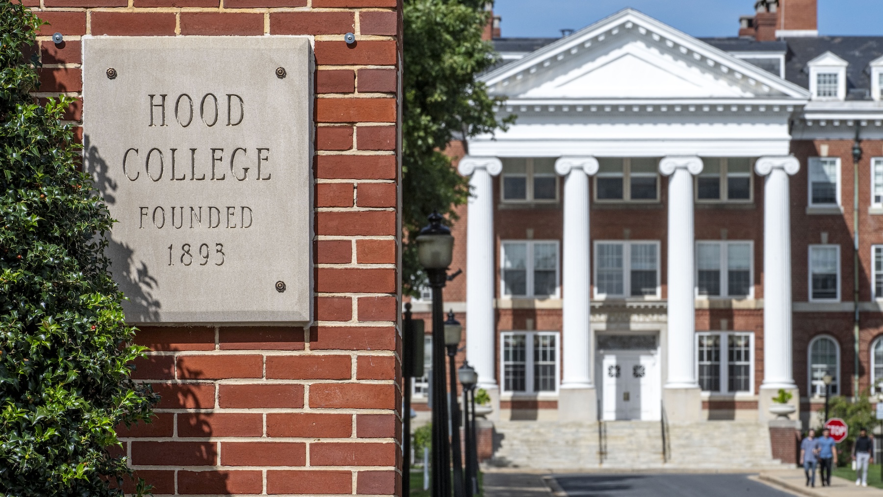 Hood College's front entrance. A sign engraved in stone reads "Hood College founded 1893" with Alumnae Hall in the background