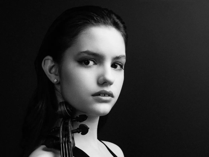 A black and white headshot of Ava Pakiam with her violin tucked under her chin