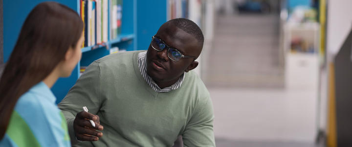 A school counselor speaking with a student in a library.